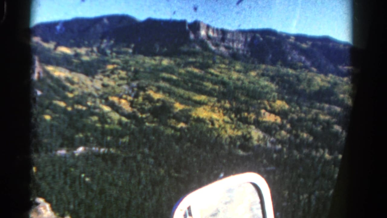 Forested Colorado mountain ridge seen through a vehicle window with a side mirror at the bottom.
