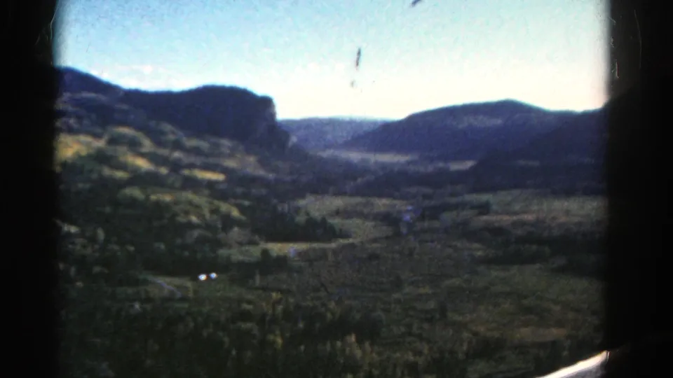 1967 Colorado 8mm frame looking across a broad valley toward dark mountain ridges from inside a vehicle.