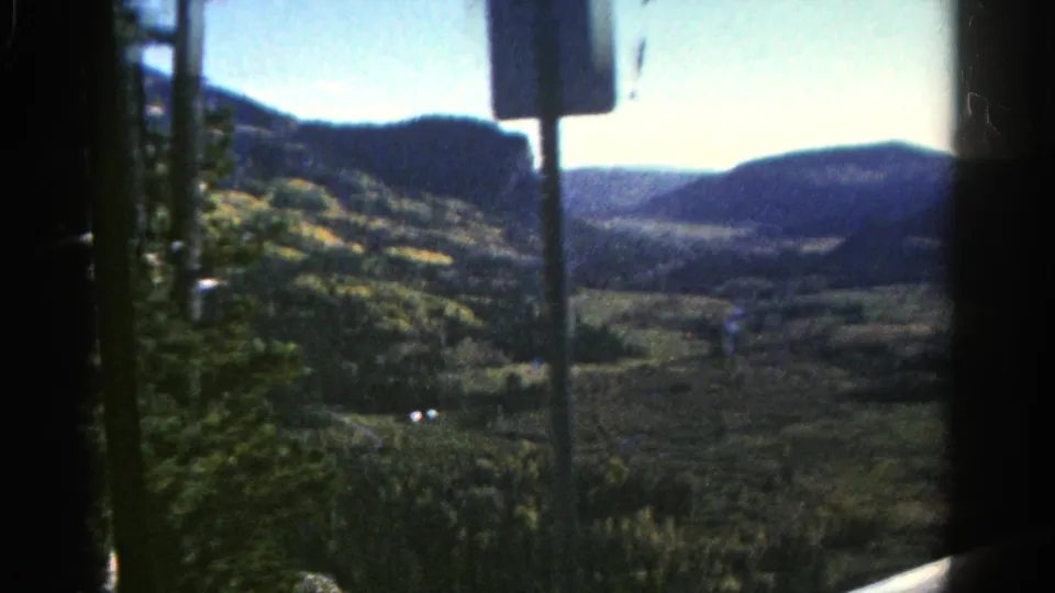 1967 Colorado 8mm frame showing a wooded mountain valley through vehicle glass, partly obscured by interior hardware.