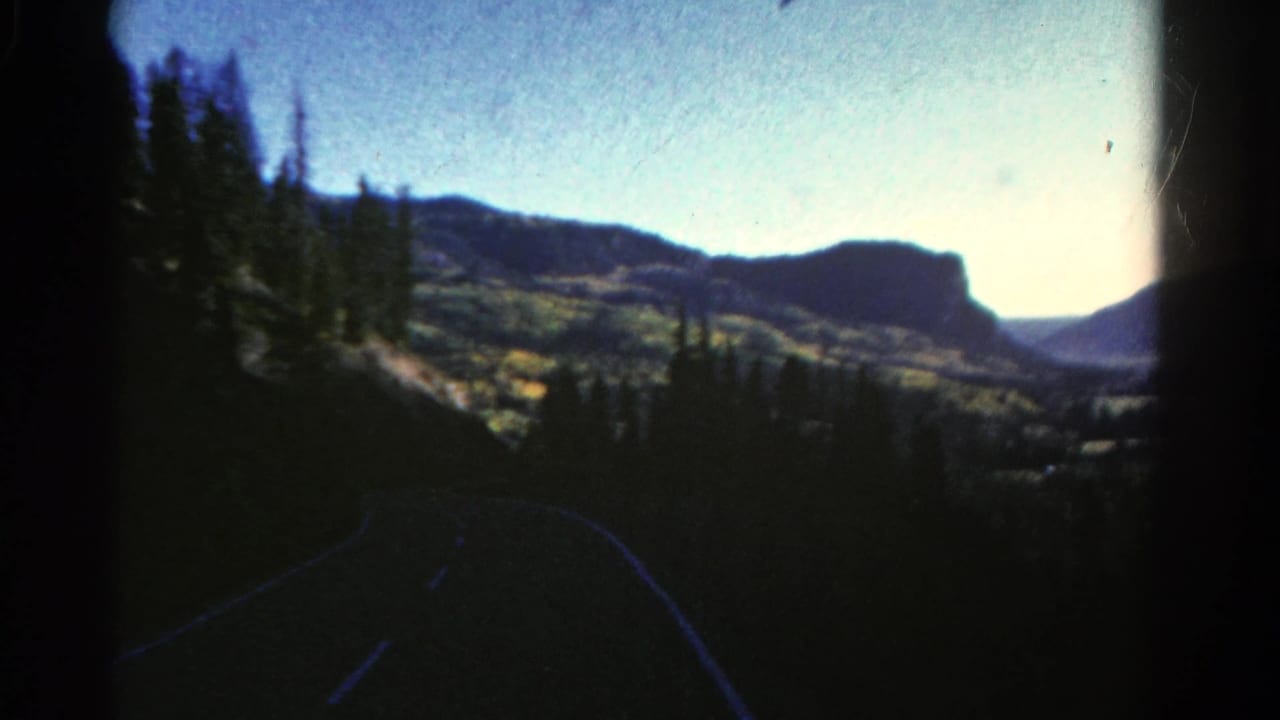 Forested mountain road with distant ridges and a bright horizon.
