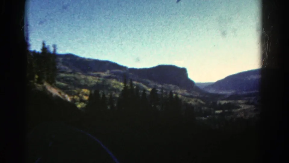 1967 Colorado 8mm frame showing a moving scenic view across pine trees and a mountain valley toward a mesa.