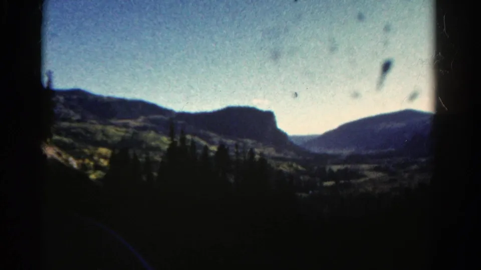 1967 Colorado 8mm frame with a distant mesa, shadowed pine foreground, blue sky, and visible film dust marks.