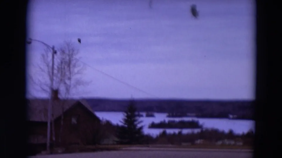 1967 8mm Detroit-area view of a lakeside house, leafless trees, utility wire, calm water, and distant islands.