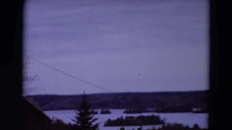 1967 8mm home-movie frame, metadata-linked to Detroit, Michigan, showing snowy water, open ground, bare trees, and a dark distant treeline.