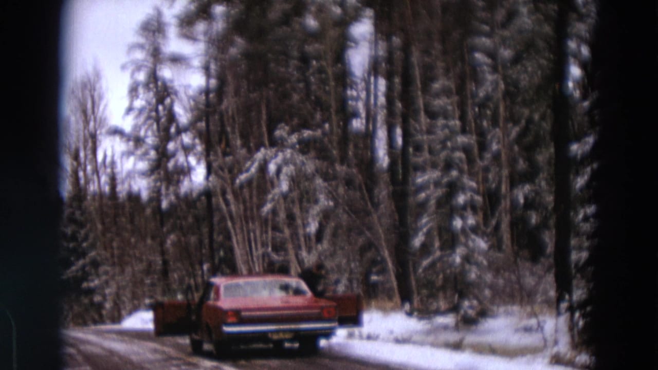 Red sedan stopped on a snowy road with open doors near a forest.
