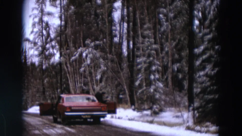 The red sedan remains stopped by a snowy forest road, with a dark-clothed person near the open rear door.