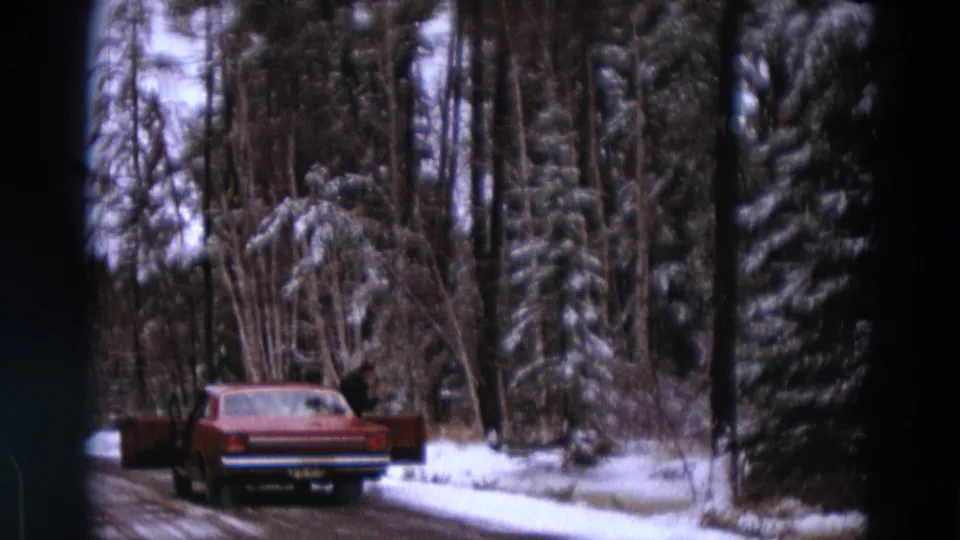 A red period car travels along a snow-lined wooded road in archival 1967 Michigan home-movie footage.