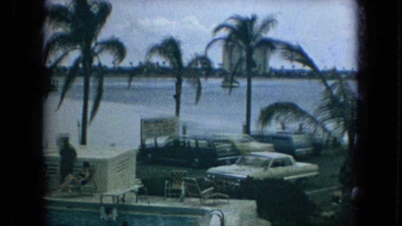 1967 Florida home-movie view of palm trees by the water, parked classic cars, a visible sign, pool steps, and distant shoreline buildings.