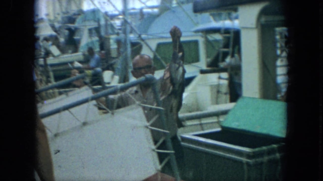Man lifts a fish on a stringer near a green cooler and boat railing.