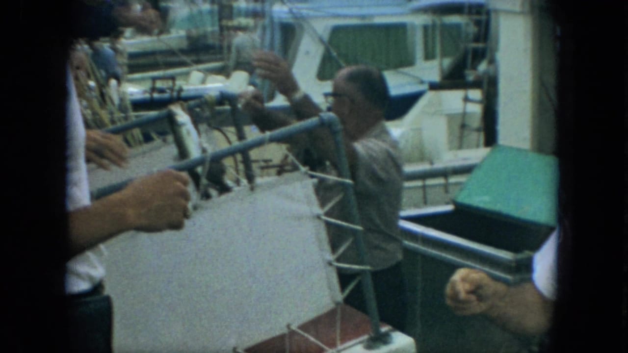 1967 Florida marina frame showing a fish being handed from a boat toward a man in glasses beside dock railings.