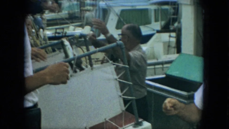 1967 Florida marina frame showing a fish being handed from a boat toward a man in glasses beside dock railings.