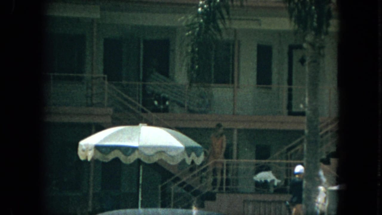 Florida motel scene from 1967 showing a large striped umbrella, outdoor corridors, stairs, palm fronds, and distant guests.