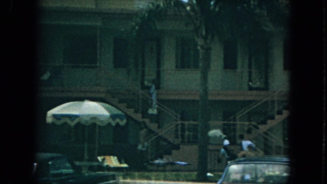 Apartment courtyard with exterior stairs, palm trees, parked cars, and a striped patio umbrella.