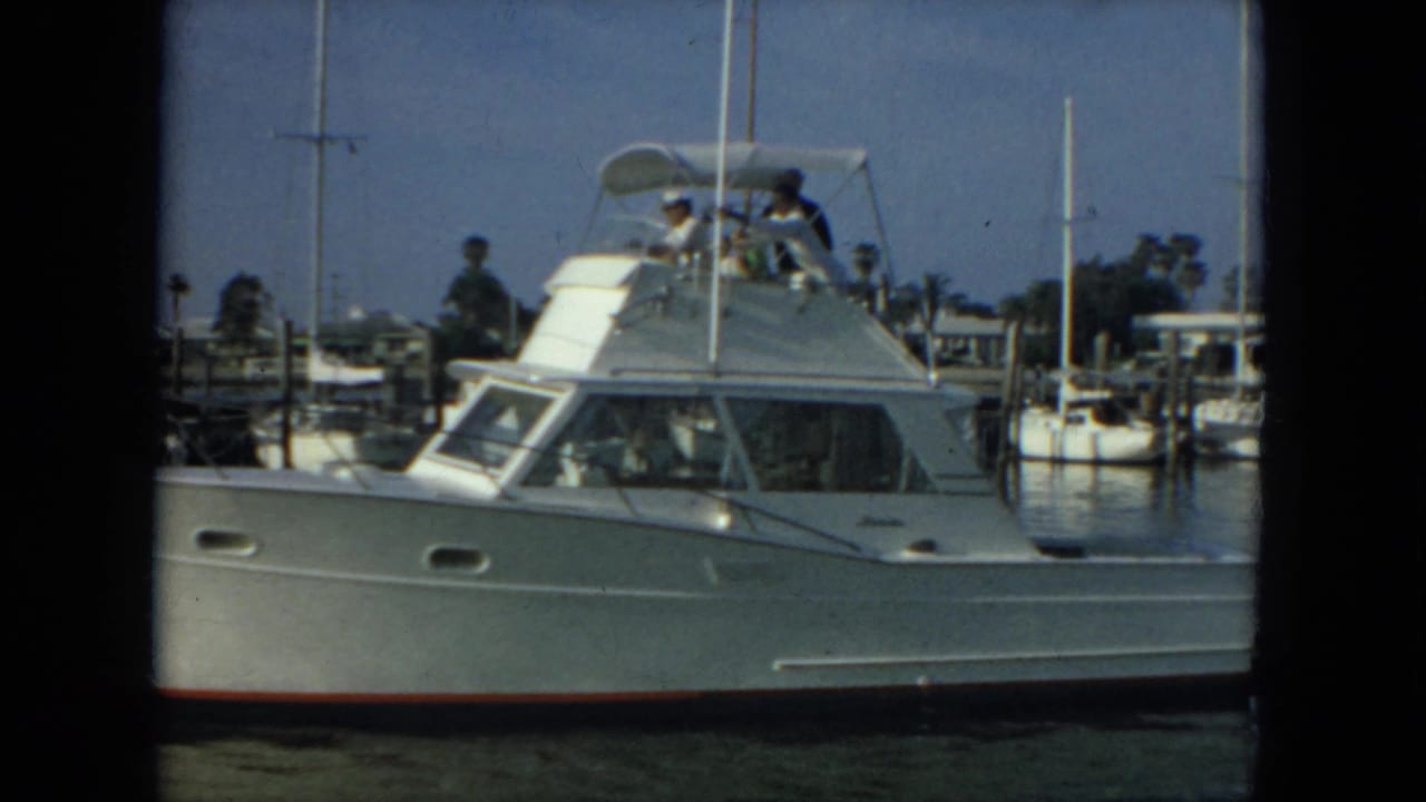 White yacht alongside marina docks with passengers visible above the cabin.