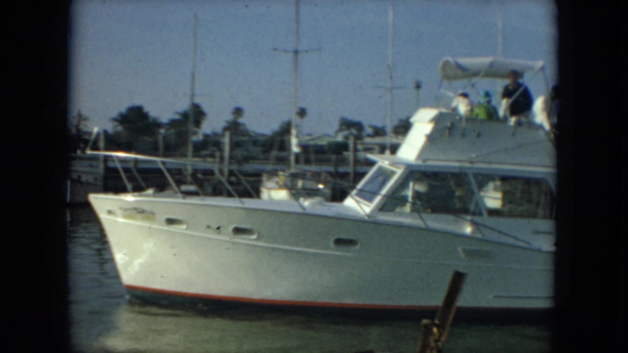 1967 Florida 8mm frame showing a white motor yacht near docked boats, with several people visible on the upper deck.