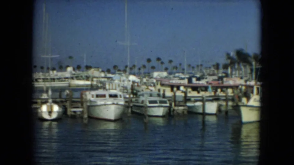 1967 Florida 8mm frame of docked boats and sailboat masts across a marina, with palm trees along the distant shore.