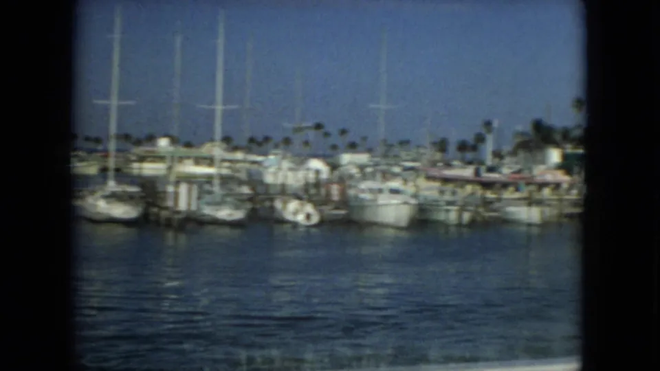 1967 Florida home-movie view across marina water toward rows of docked boats, tall masts, and palm trees.