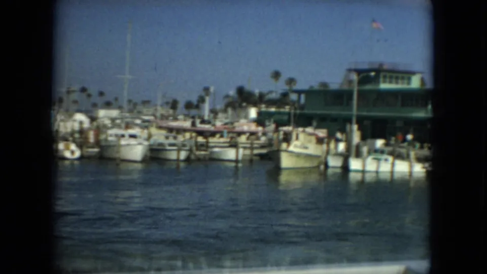 Florida marina frame from 1967 showing moored boats, a green waterfront building, palm trees, and an American flag.