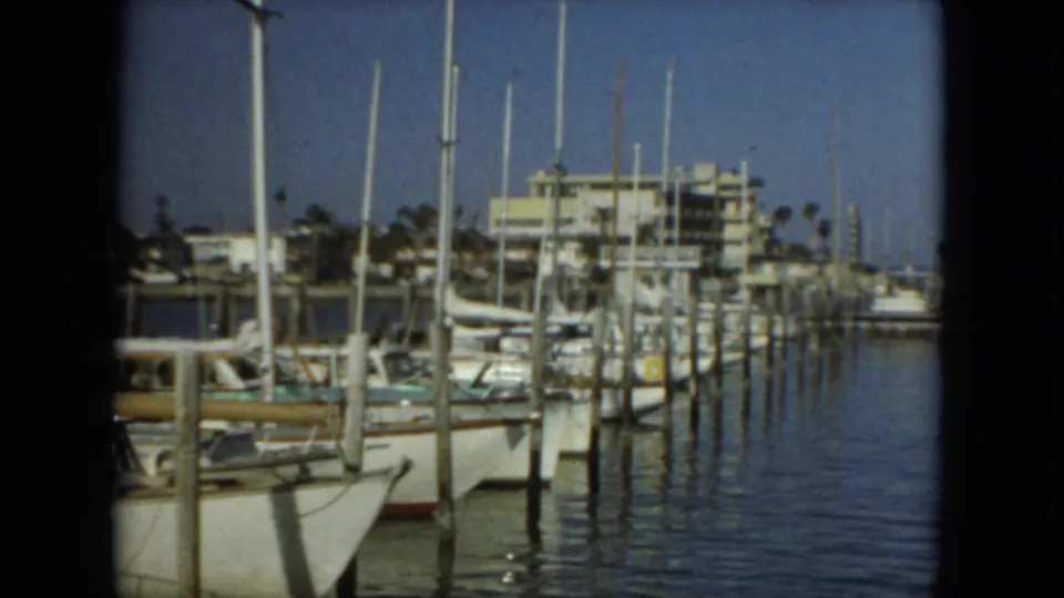 1967 Florida 8mm frame showing moored sailboats, dock pilings, masts, calm marina water, and low waterfront buildings.