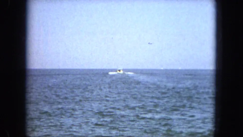 1967 Florida 8mm frame showing a distant motorboat moving across open blue water beneath a pale horizon.