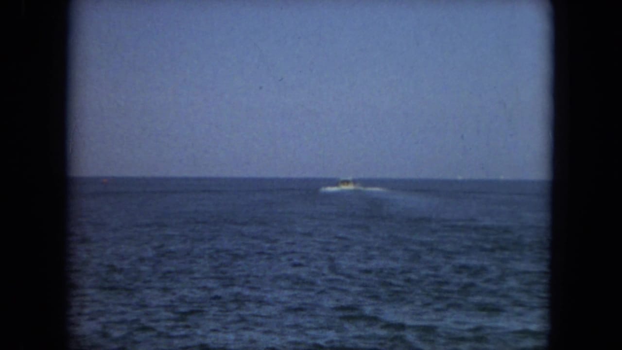 Distant motorboat on open water near the horizon, framed by dark film edges.