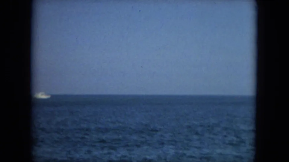 A small white boat sits near the distant horizon over blue Florida water in the final 1967 8mm frame.