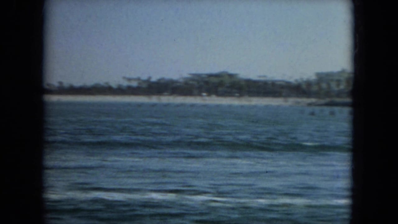 Open water and distant beach with low shoreline buildings under a hazy sky.