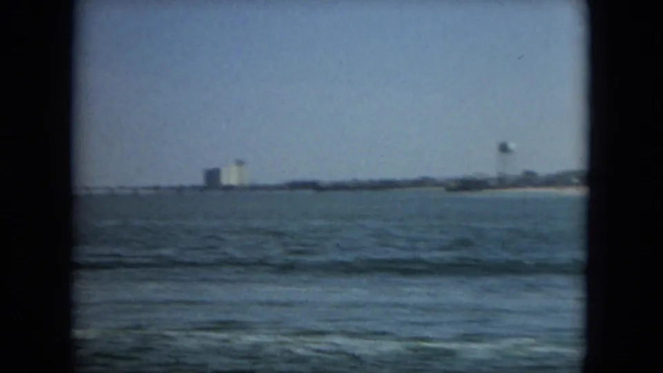 1967 Florida 8mm frame showing open sea in the foreground and a distant beach town with a water tower on the horizon.