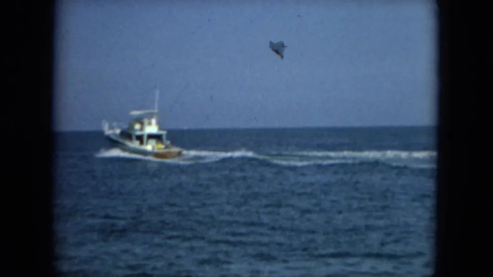 1967 Florida 8mm frame showing the motorboat farther from camera on blue water with a long wake behind it.