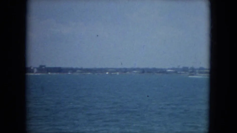 1967 Florida 8mm frame of a low shoreline across open water, with a small white boat near the horizon.