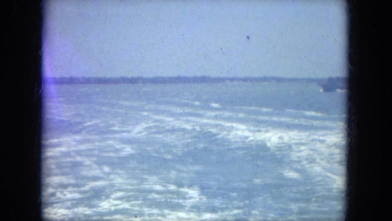 Open water seen from a moving boat with a low distant shoreline and dark film gate edges.