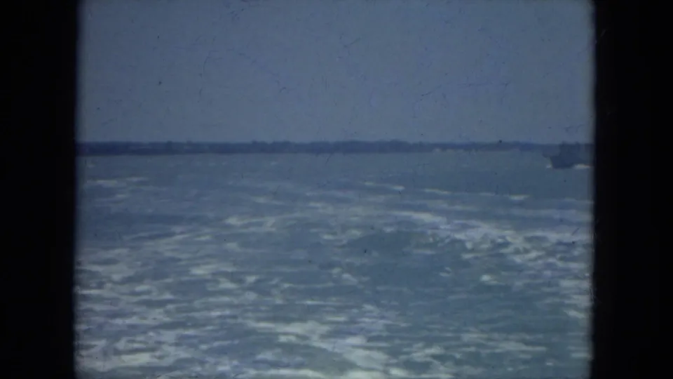 Foamy wake from a moving boat crosses open Florida water, with a faint vessel near the horizon in faded 8mm color.