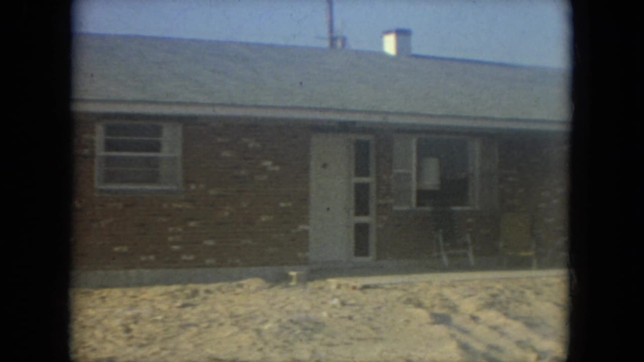 Brick house exterior with porch area, white door, window, and chairs near the wall.