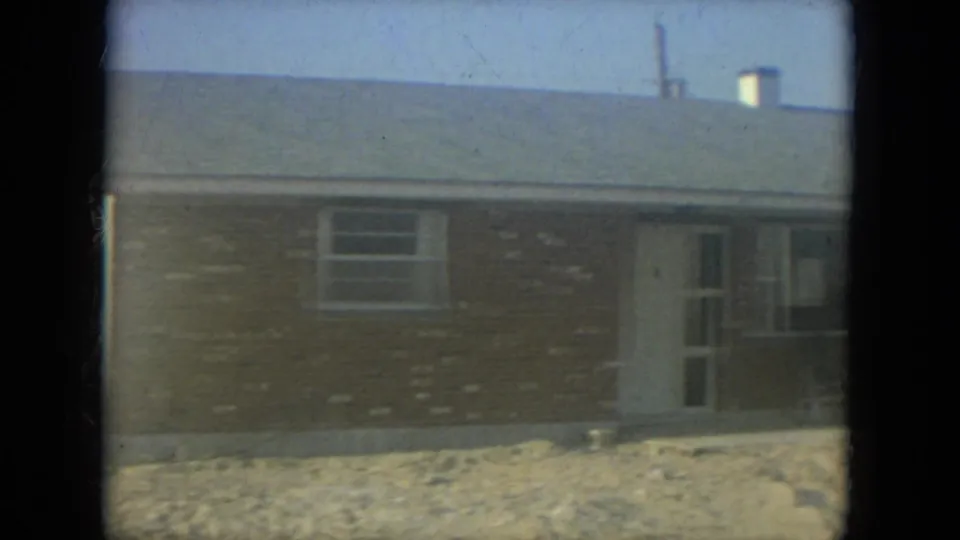 1967 Florida 8mm frame showing the brick house facade, white door, window, and porch chair during a slow exterior pan.
