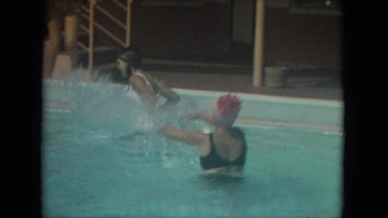 Women in swimsuits play in a Florida swimming pool in 1967, with a pink building and exterior stairs behind them.