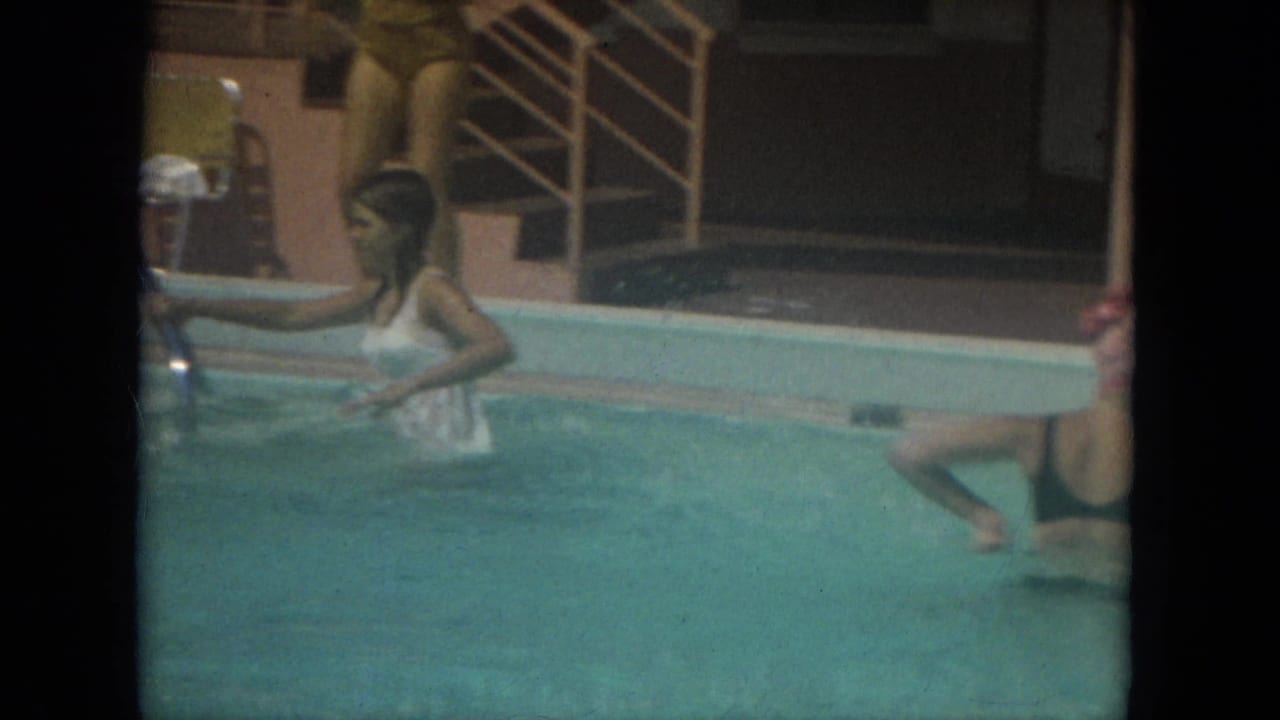 A woman in a white dress wades in a Florida pool while other women stand nearby during a 1967 home movie scene.
