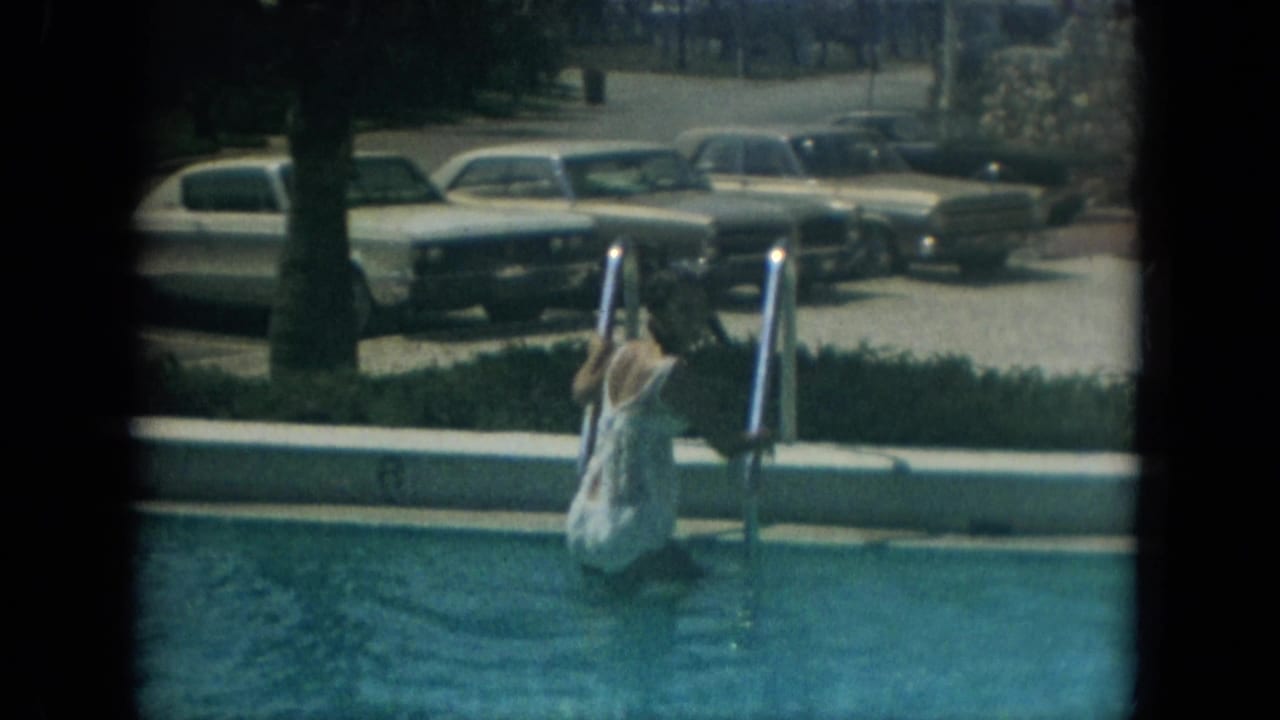 Woman in a white cover-up steps down a swimming pool ladder with parked cars behind her.
