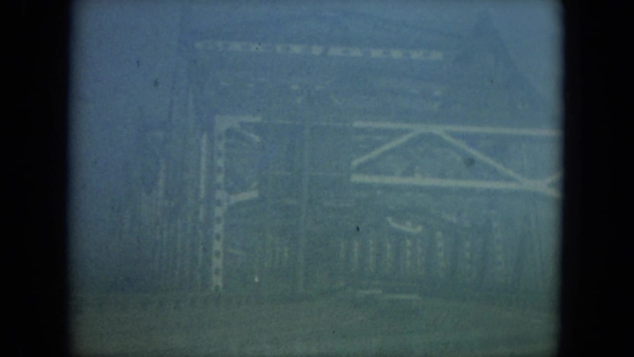 1967 Florida 8mm frame looking through a dark car window toward hazy bridge-like railings and exterior structure.
