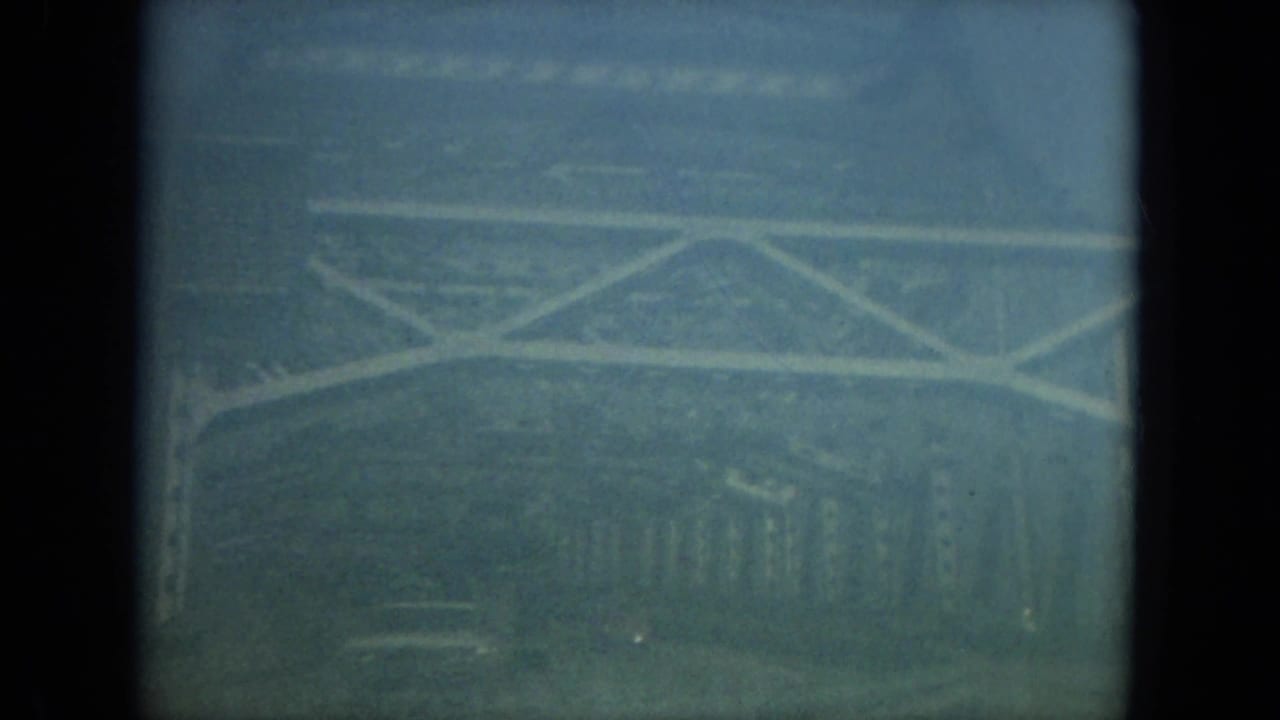 1967 Florida home-movie frame with a divided car-window view of pale bridge-like bracing and a foggy roadway area.