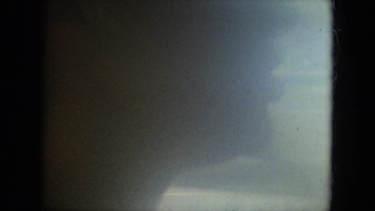 Dark, soft 8mm frame with greenish tones, grain, dust, and a bright patch near the lower right.