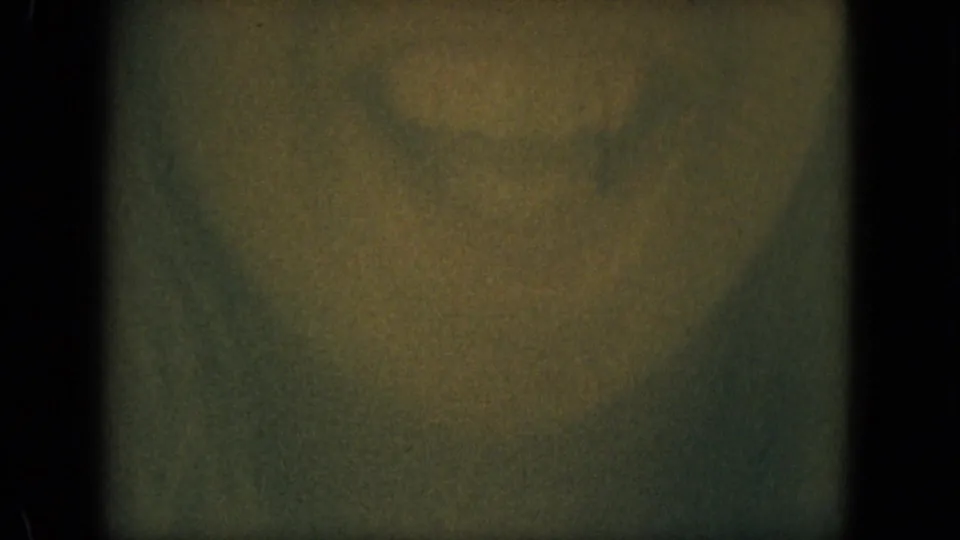 Dim 1967 Florida 8mm frame with grain, green shadowing, a faint warm central blur, and no identifiable person or setting.