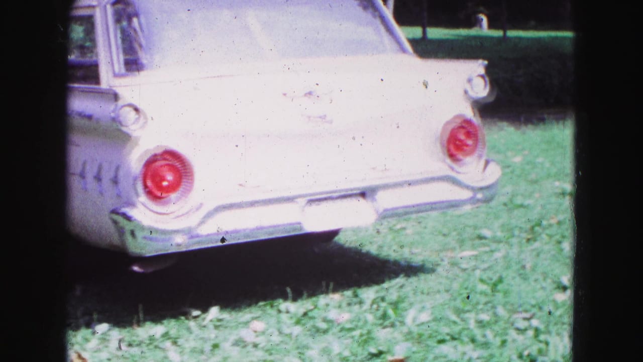 Rear corner of a white station wagon parked on grass with round red taillight.