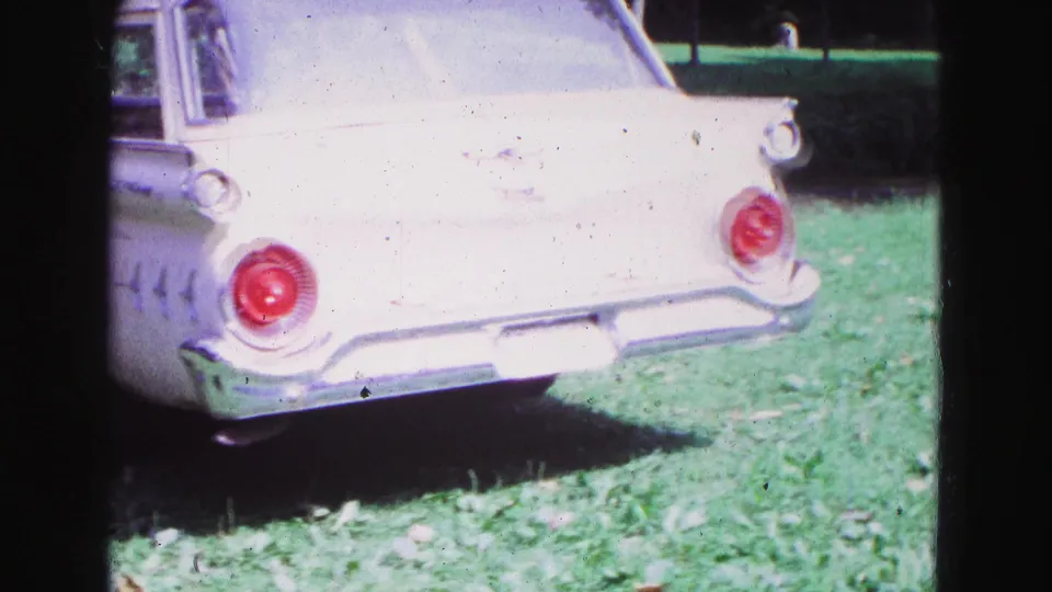 1967 Galena, Illinois home-movie frame showing the rear corner of a white American station wagon parked on a grassy lawn.