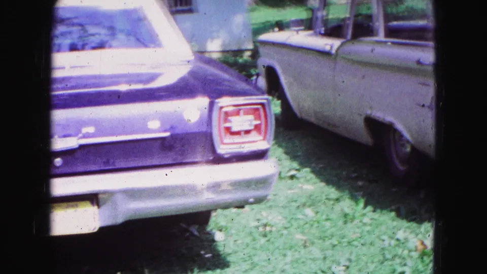 Purple Ford Falcon rear and a white station wagon parked on grass in 1967 Galena, Illinois footage.