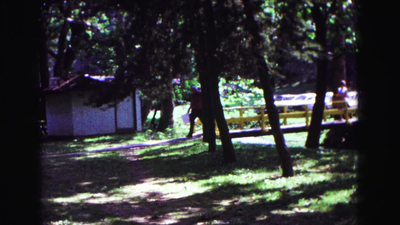 Trees and a white building frame a yellow railing with people in the distance.
