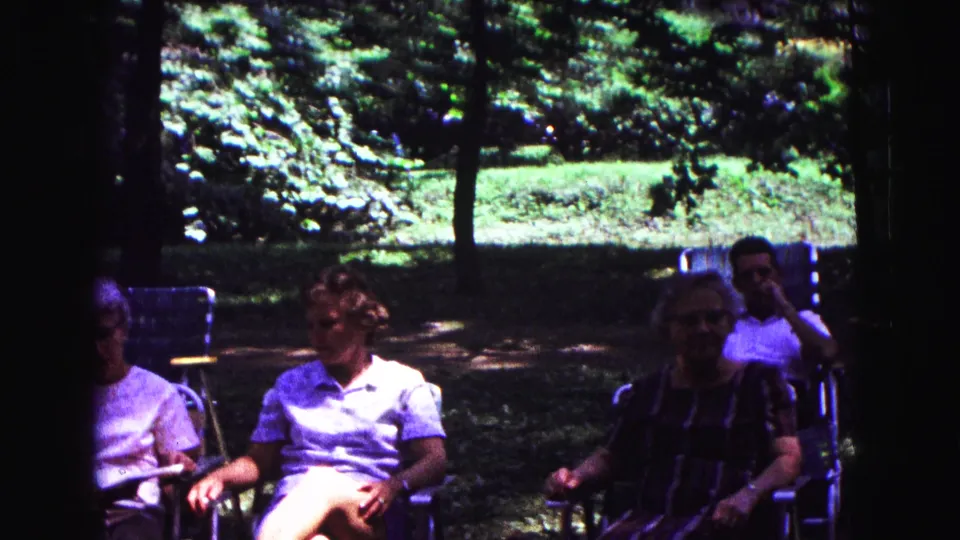 Adults relax in folding lawn chairs at a Galena park in 1967, framed by trees, grass, and bright sunlight.