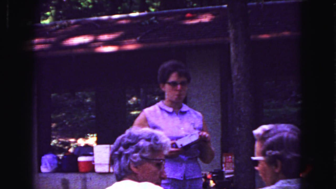 Woman holds a small item at the counter as older patrons sit in the foreground.
