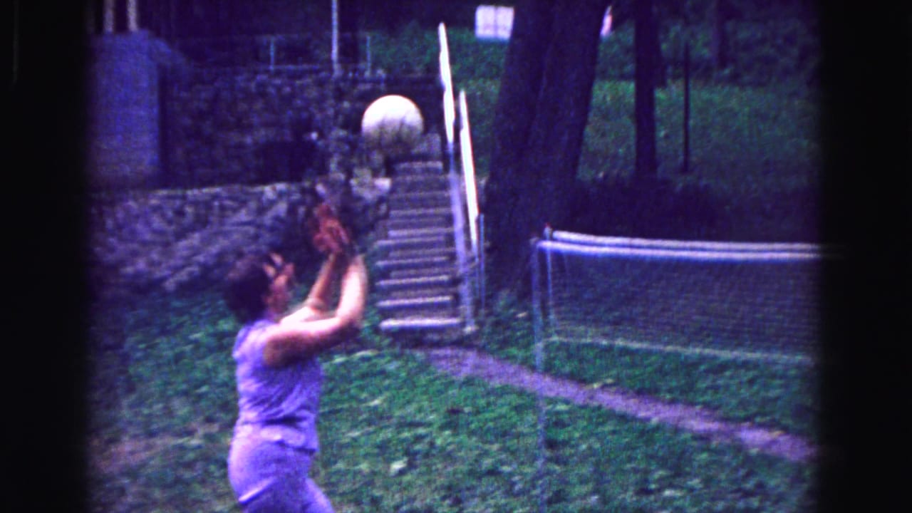 1967 Galena, Illinois home-movie frame showing a woman in purple playing volleyball on a grassy backyard court.