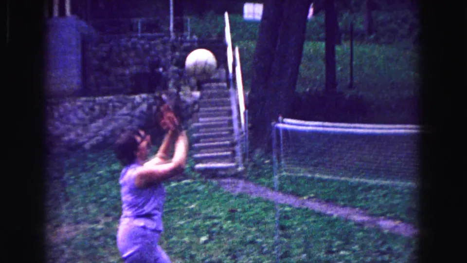 1967 Galena, Illinois home-movie frame showing a woman in purple playing volleyball on a grassy backyard court.
