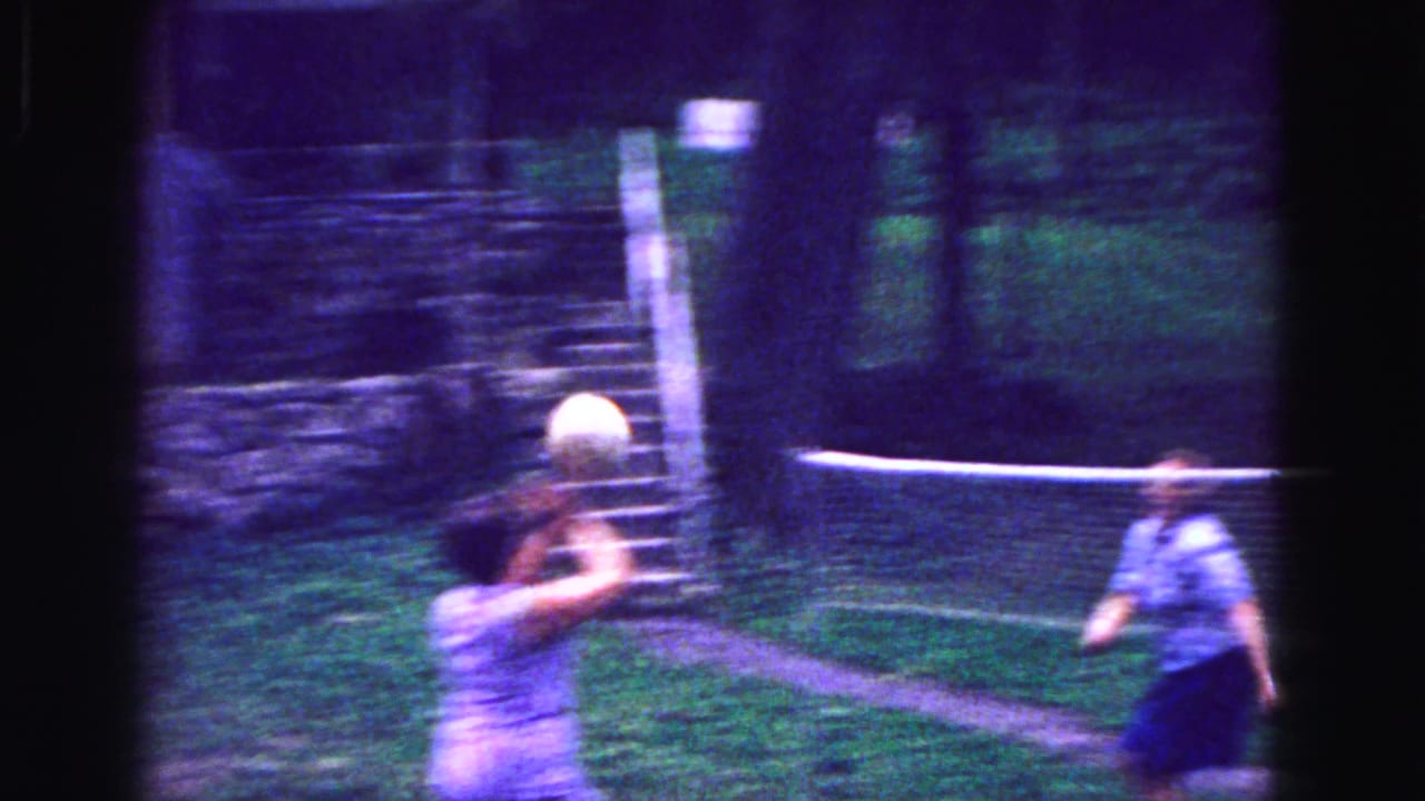 Woman in a light dress hits a volleyball over a backyard net.